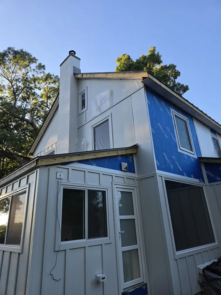 White board and batten siding installation around a chimney at dusk