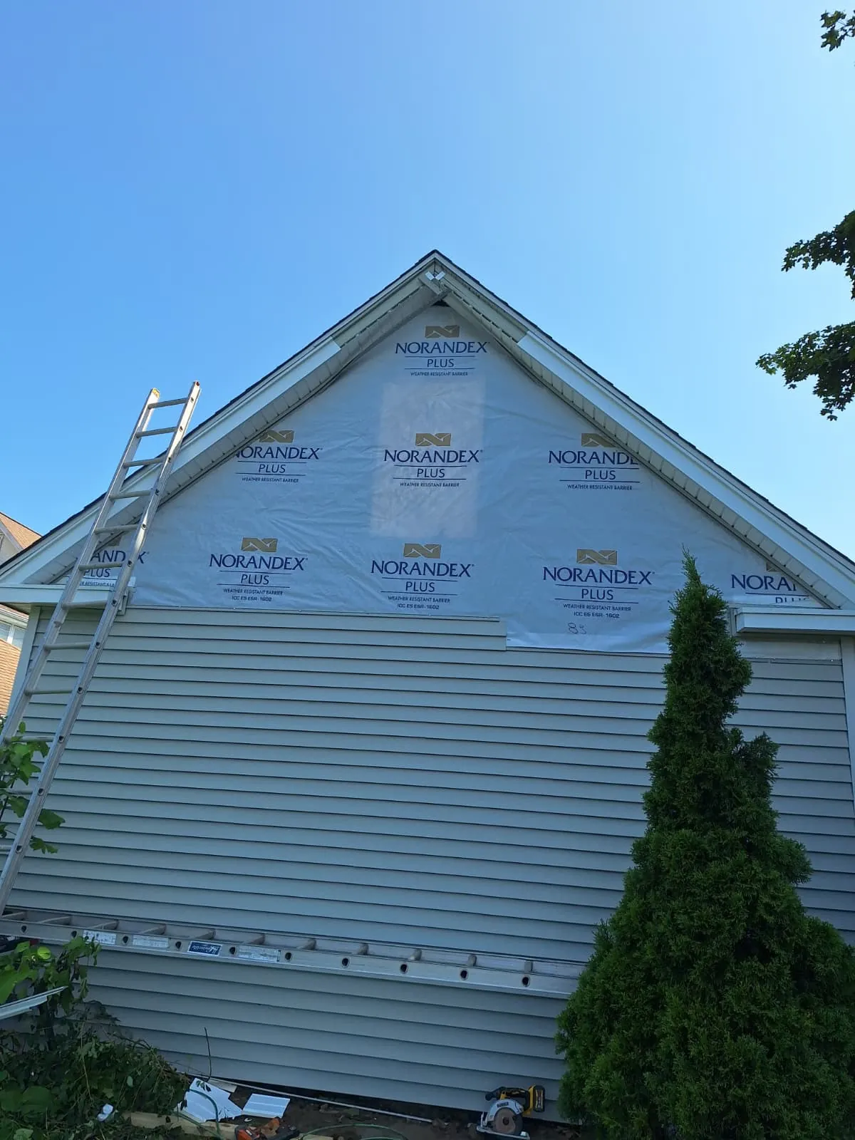 House wrap and siding installation in progress on a gable with ladder